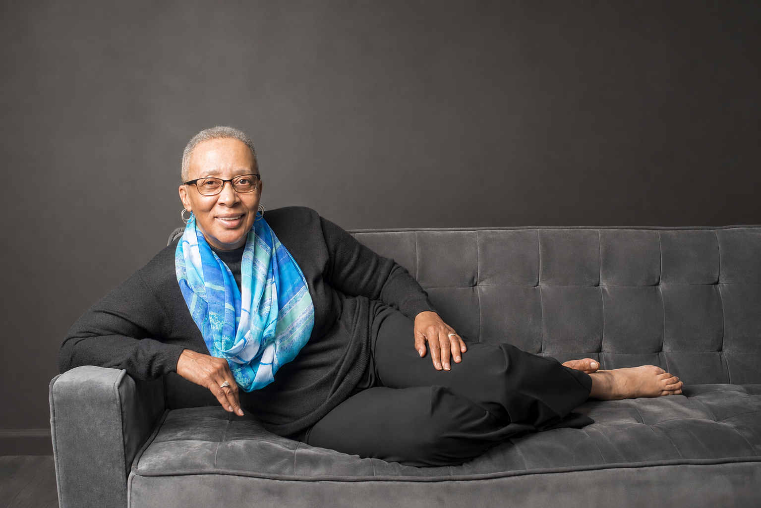 Portrait of Crystall Gates relaxing on a charcoal sofa in a vivid blue scarf